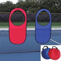 two red and blue doors are on the side of a tennis court, with trees in the background