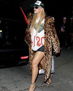 a woman in leopard print coat and hat walking down the street with her hand on her hip