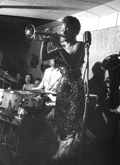 a black and white photo of a woman in a sequin dress playing the trumpet