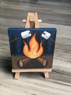 an easel with a painting on it that has a campfire and two marshmallows