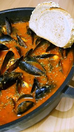 mussels and bread in a red sauce on a wooden table