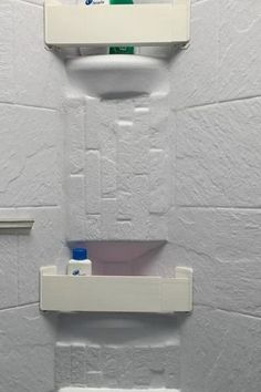 two white shelves with toothpaste on them against a wall in a bathroom stall