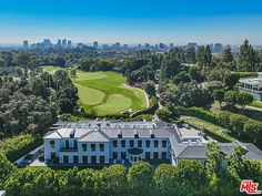 an aerial view of a large white mansion with trees in the foreground and buildings in the background