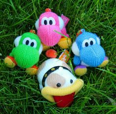 four knitted toys are laying in the grass together, one is wearing a hat