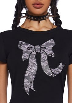 This graphic tee has a stretchy knit construction, short sleeves, and a textured lace bow graphic on the front with stud detailing. Black Tops With Bow For Night Out, Black Bow Top For Night Out, Black Bow Tops For Night Out, Edgy Party T-shirt With Graphic Print, Edgy Graphic Print T-shirt For Party, Edgy Crew Neck T-shirt For Party, Grunge Short Sleeve Party Tops, Short Sleeve Cotton T-shirt With Lace Trim, Grunge Short Sleeve Tops For Party