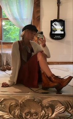 a woman sitting on the floor taking a selfie with her cell phone and wearing boots