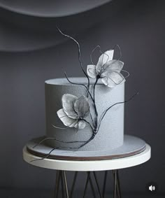 a white and gray cake with flowers on it sitting on a table next to a black wall