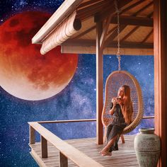 a woman sitting in a hanging chair on a porch next to a full moon and red blood moon