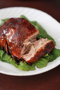 a white plate topped with meat and lettuce on top of a wooden table