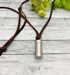 a necklace with a metal tube on a brown cord next to some flowers and leaves