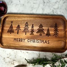 a wooden cutting board with christmas trees engraved on it and a glass of wine next to it