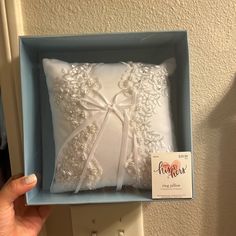 a white pillow in a blue box with a ribbon on the side and a name tag attached to it