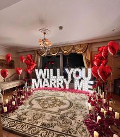 a room with many red balloons and candles on the floor in front of a large sign that says will you marry me?