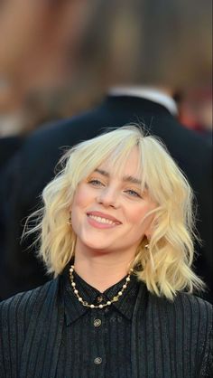 a woman with blonde hair smiling and wearing a black shirt at the red carpet event