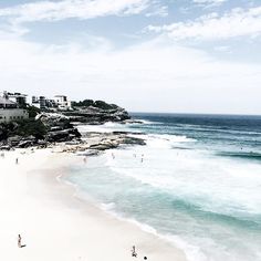 people are walking on the beach and in the water near some buildings with white balconies