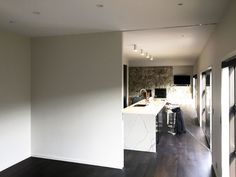 an empty kitchen with white walls and wood flooring is seen from the hallway to the living room