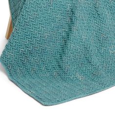 a green knitted blanket folded on top of a wooden chair