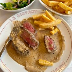 a plate with steak and french fries on it, next to a bowl of salad