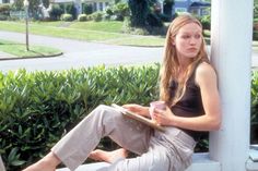 a young woman sitting on a porch with her feet propped up against the wall and reading