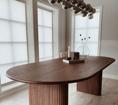 a large wooden table sitting in the middle of a room next to two tall windows