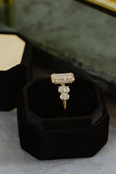 an engagement ring in a black velvet box on a table next to other jewelry items