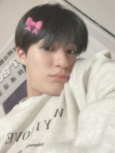 a young man with a pink bow in his hair is looking at the camera while wearing a white sweater