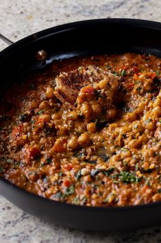 a skillet filled with food on top of a marble countertop next to a spoon