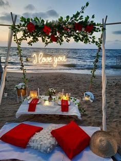 a table set up on the beach with candles and flowers in front of it that says i love you