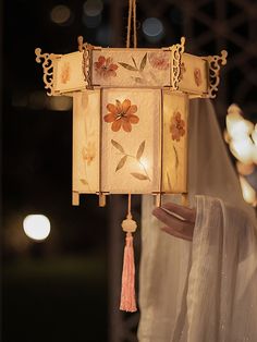 a lamp hanging from a ceiling with flowers on it and tassels attached to the lights