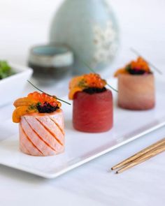 three sushi on a white plate with chopsticks