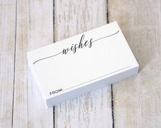 a white business card sitting on top of a wooden table with the word wishes written in cursive writing