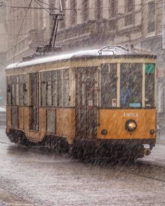 a yellow trolley car traveling down a rain soaked street