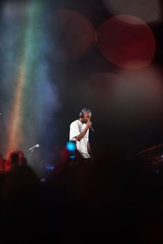 a man standing on top of a stage next to a rainbow colored light behind him