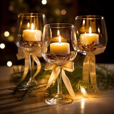 three wine glasses with candles in them sitting on a table next to evergreen branches and lights