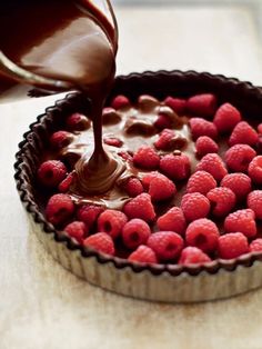 a chocolate tart with raspberries is being drizzled