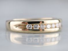 a gold wedding ring with five diamonds on it's side, sitting on a reflective surface