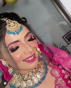 a woman in a pink dress with gold jewelry on her head and nose ring around her neck