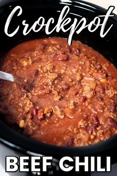 a crockpot filled with beef chili on top of a white table next to a spoon