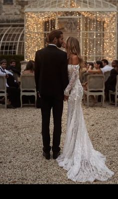 a bride and groom standing in front of a building with fairy lights on the walls