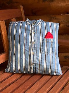 a blue striped shirt with a red heart on it sits on a wooden bench next to a pillow