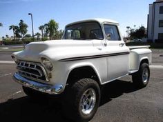 an old white pickup truck parked in a parking lot with palm trees and buildings in the background