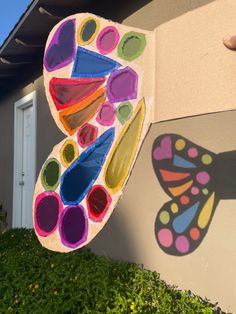 a colorful butterfly painted on the side of a building next to a green planter