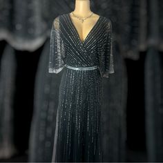 This Is A Sophisticated Black Evening Gown Adorned With Shimmering Sequin Stripes That Create A Radiant, Starburst Effect. The Flowy, Sheer Cape Sleeves Add A Graceful Touch, While The Metallic Belt Cinches The Waist For A Flattering Silhouette. Perfect For Formal Occasions Or Elegant Parties. Elegant Gray V-neck Evening Dress, Elegant Black Floor-length Mother Of The Bride Dress, Black Floor-length Mother Of The Bride Dress, Black Maxi Mother Of The Bride Dress For Wedding, Elegant Black Mother Of The Bride Evening Dress, Fitted Floor-length Black Mother Of The Bride Dress, Glamorous Black Evening Dress For Mother Of The Bride, Glamorous Black Mother Of The Bride Evening Dress, Elegant Gray Evening Dresses