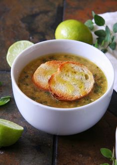 a white bowl filled with soup next to limes and two slices of bread on the side