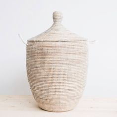 a large woven basket sitting on top of a wooden table next to a white wall