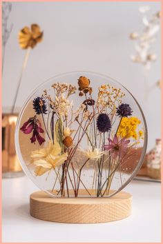 Pressed flowers encased in a round, clear resin on a wooden stand. Dried Flower Epoxy Resin, Epoxy Resin Dried Flowers, Simple Resin Art Ideas, Resin Art With Flowers, How To Dry Flowers For Resin, Pressed Flower Projects, Resin Products Ideas, Crafts With Dried Flowers, Preserve Flowers In Resin