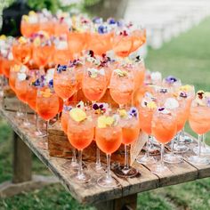 there are many glasses on the table with different types of drinks in them and one is filled with orange liquid