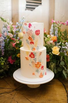 a three tiered white cake with colorful flowers on it