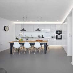 a kitchen and dining area with white chairs, an island table and a clock on the wall