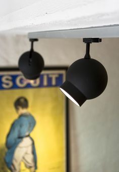 two black lamps hanging from the ceiling in front of a painting with a woman's image on it